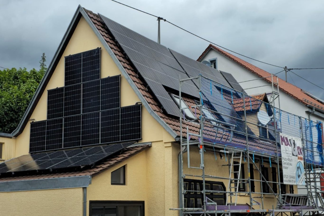 Photovoltaikinstallationen Haus mit Solarpanelen und Baustellengerüst, unter bewölktem Himmel.