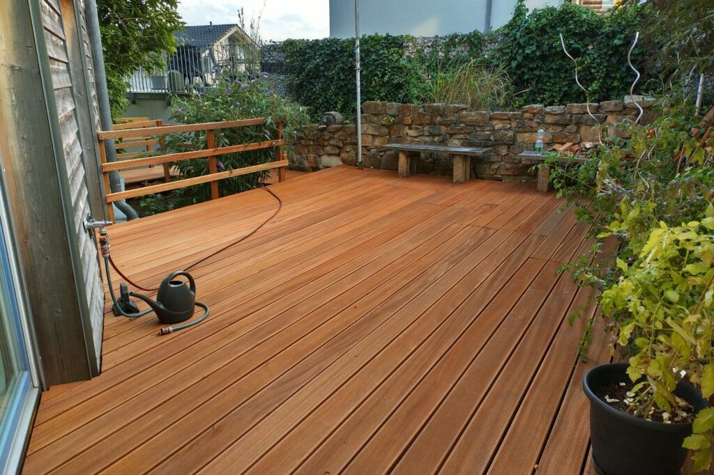 Holzbau Hölzerne Terrasse mit Pflanzen und einer Steinmauer im Hintergrund.