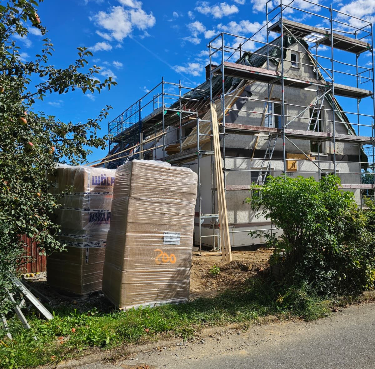 Dachsanierungen Baustelle eines Hauses mit Gerüst und Baustellenmaterial im Vordergrund.