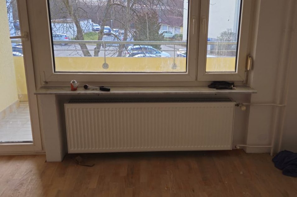 Montagearbeiten Heizkörper unter einem großen Fenster mit Blick auf einen Balkon.